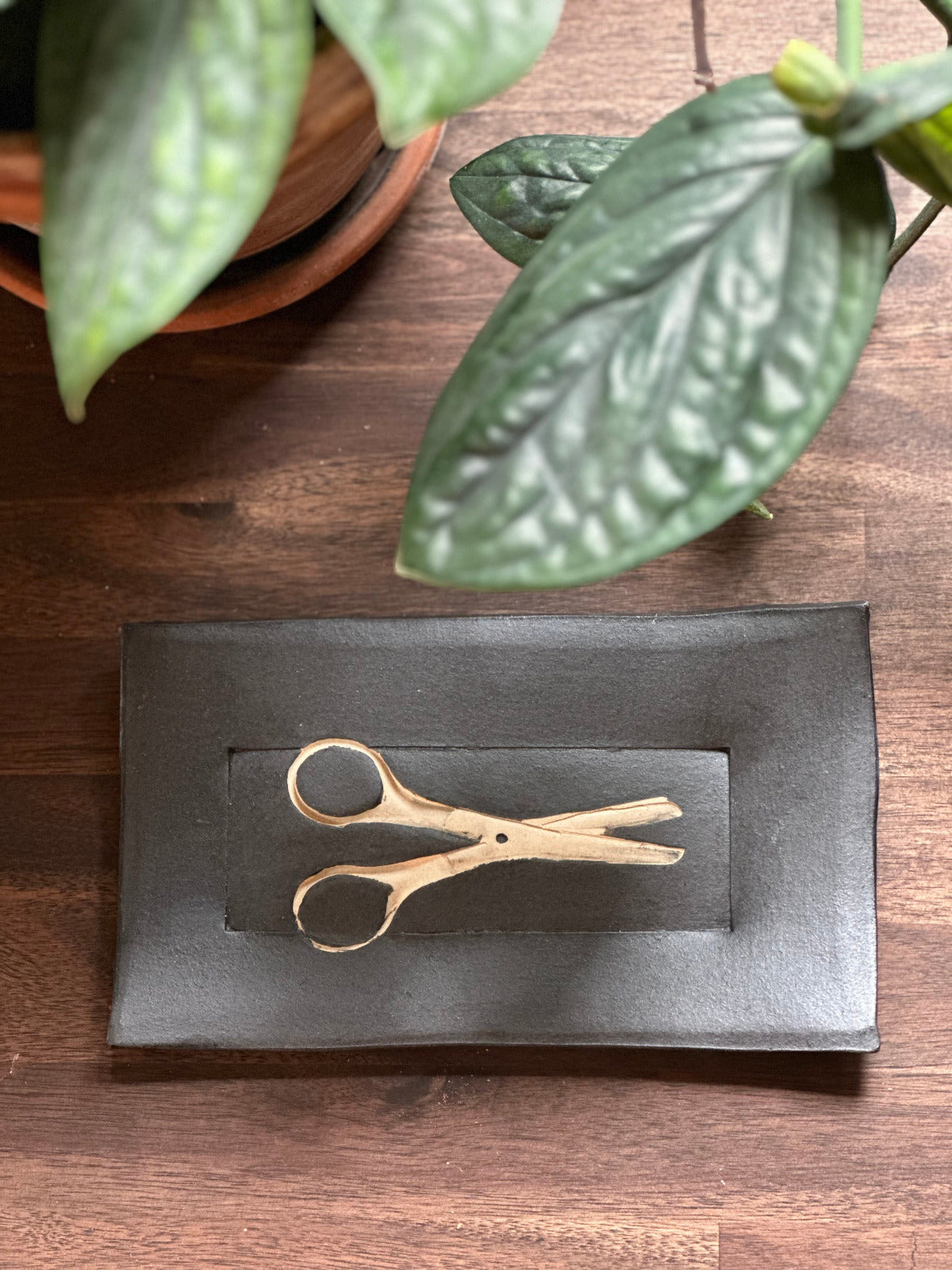 a pottery tray in black with a pair of scissors design impressed into the pottery