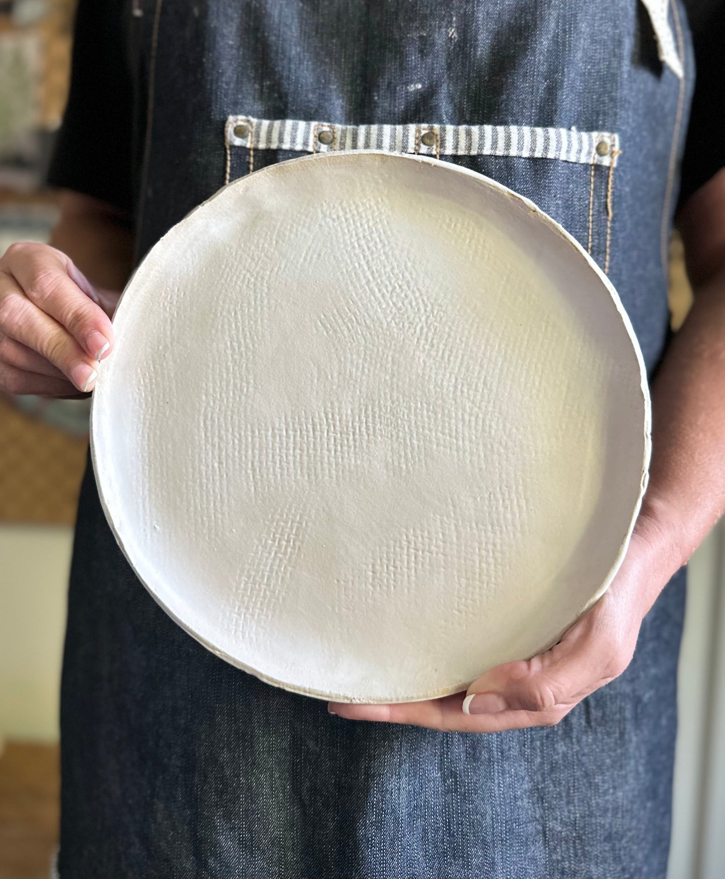 Someone holding handmade pottery dinner plate in matte white with burlap texture.