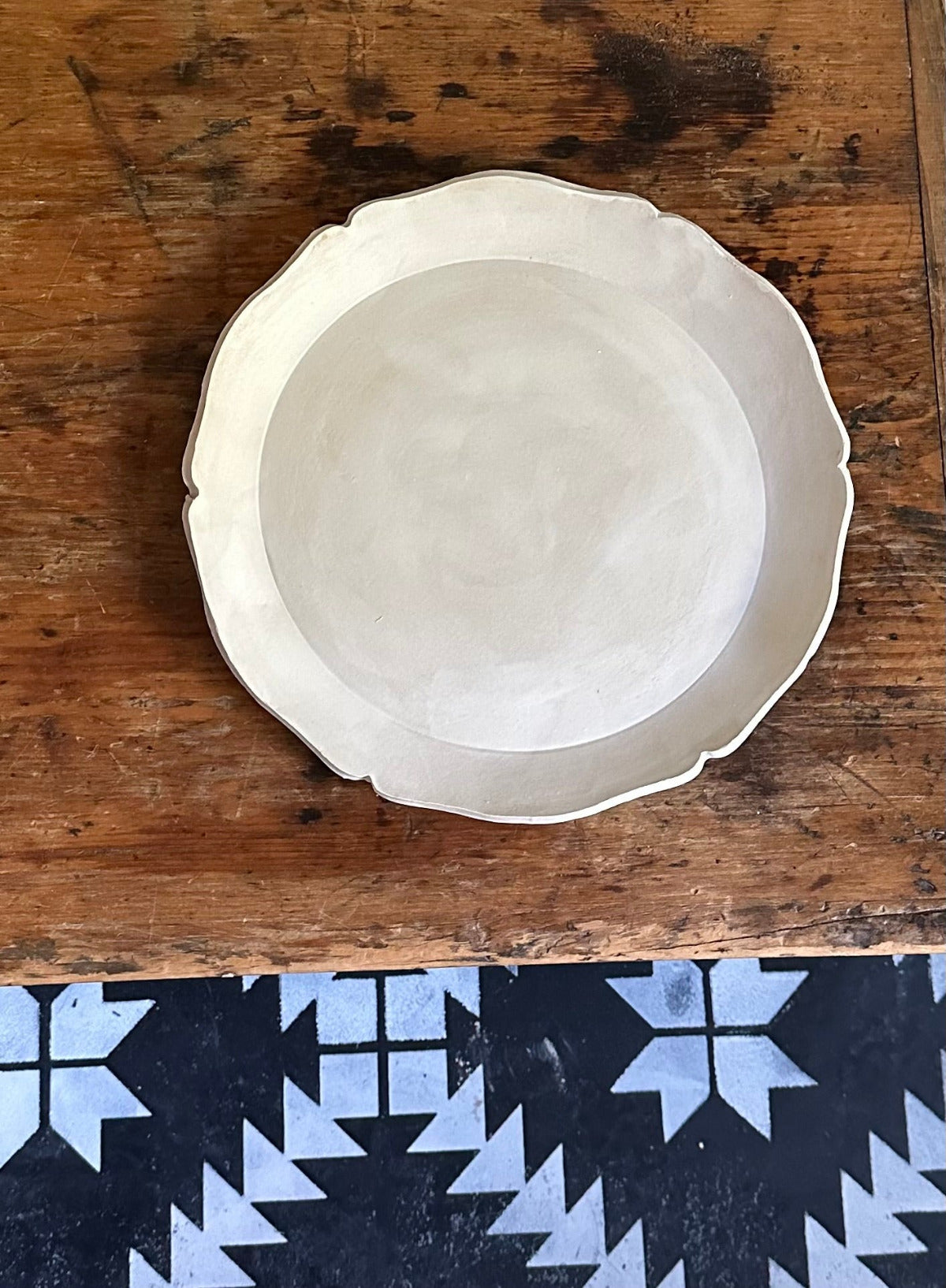 Matte white plate with scalloped edge sitting on wood chest