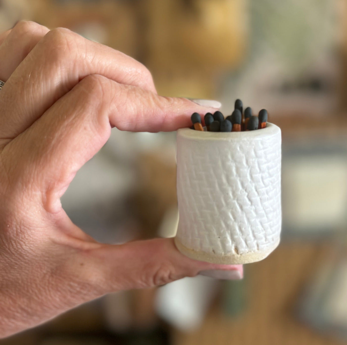 A hand holding a small, white ceramic matchstick/toothpick holder with some matchsticks and toothpicks inside.