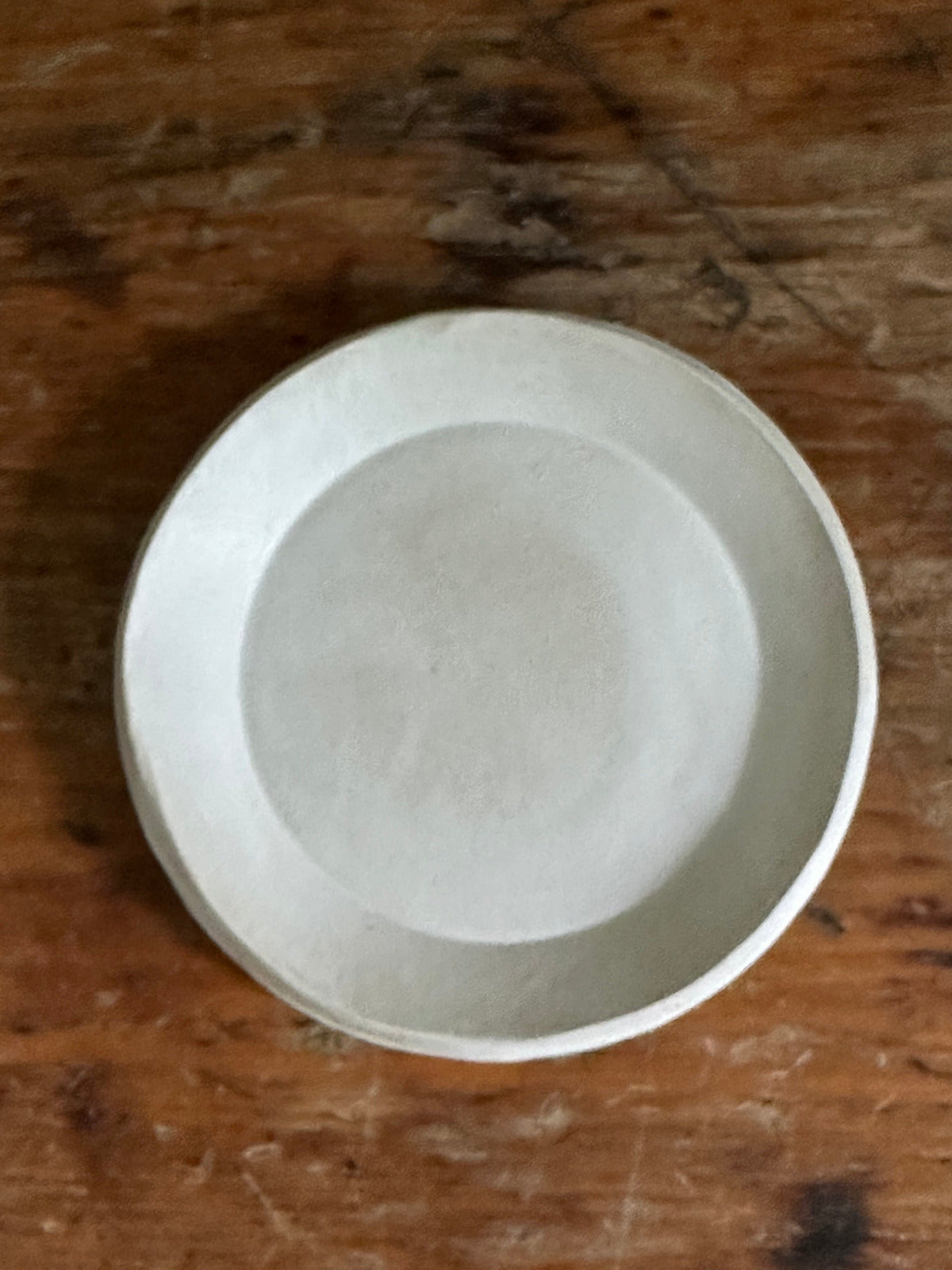 A matte white small round ceramic dish placed on a wooden surface.