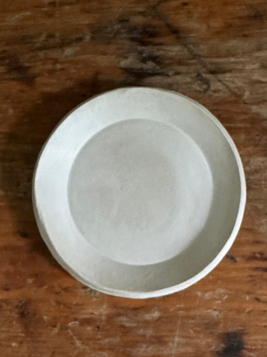 A matte white small round ceramic dish placed on a wooden surface.