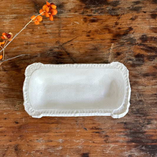 White ceramic dish on a wooden surface with a small branch of orange flowers.