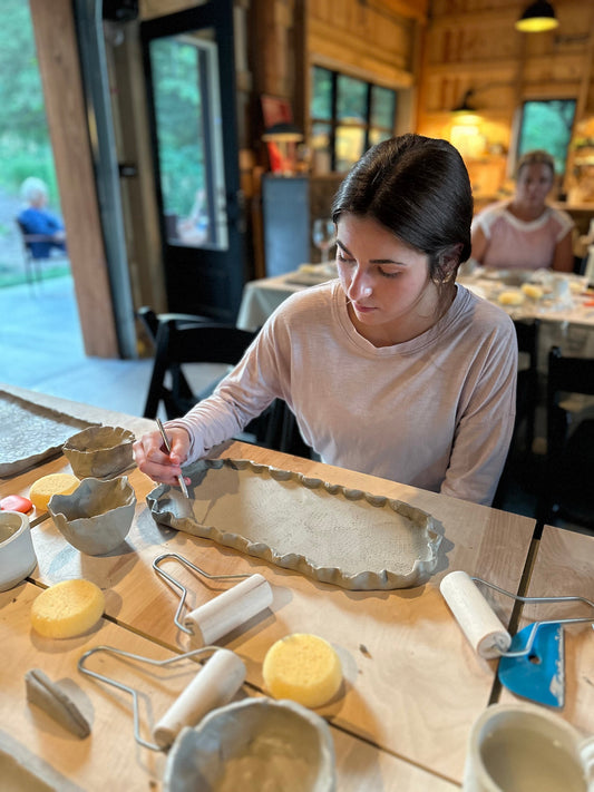 Woman working with clay on a wooden table in a rustic setting