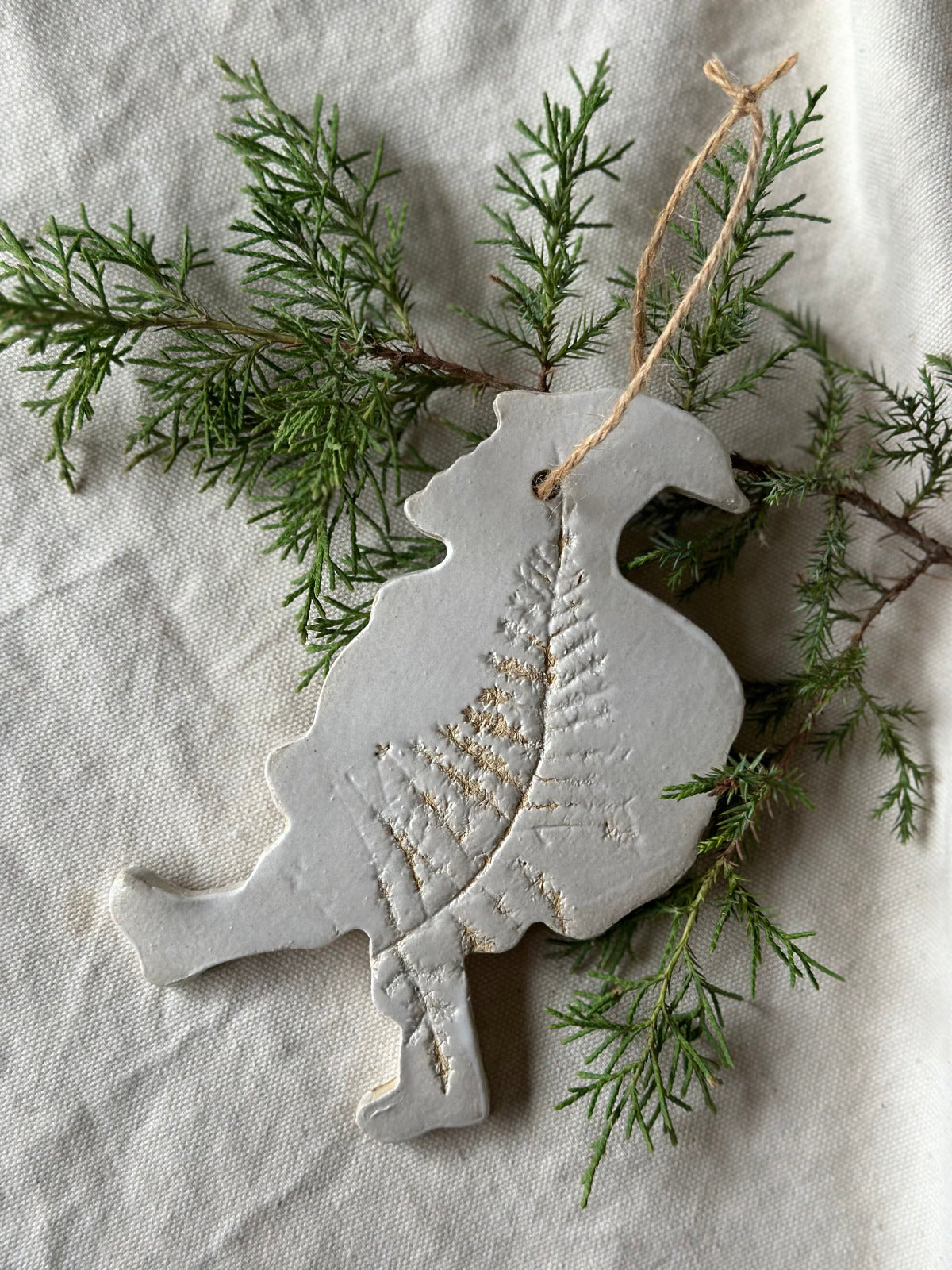 Decorative ceramic dove ornament with textured surface on a branch with green leaves.