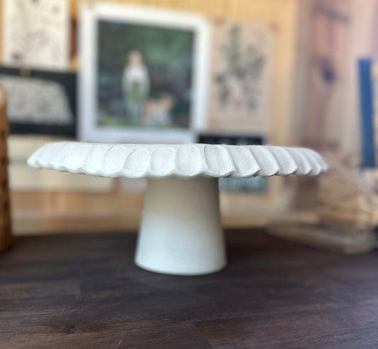 White ceramic cake stand on a wooden surface with a blurred background