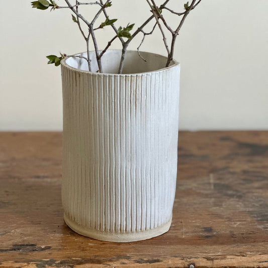 A matte white, vertically lined large flower vase on a wooden surface.