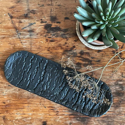 Oval ceramic tray with a tree trunk texture in a black matte glaze.
