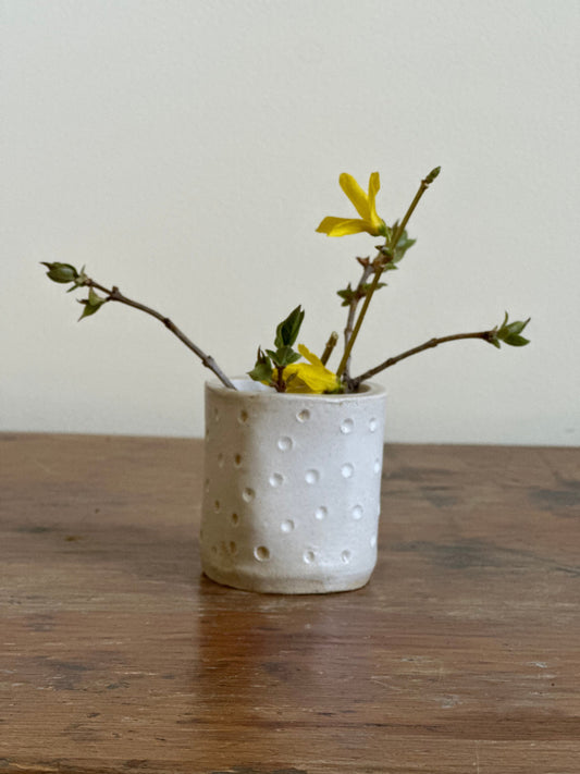 White textured vase with yellow flowers on a wooden surface