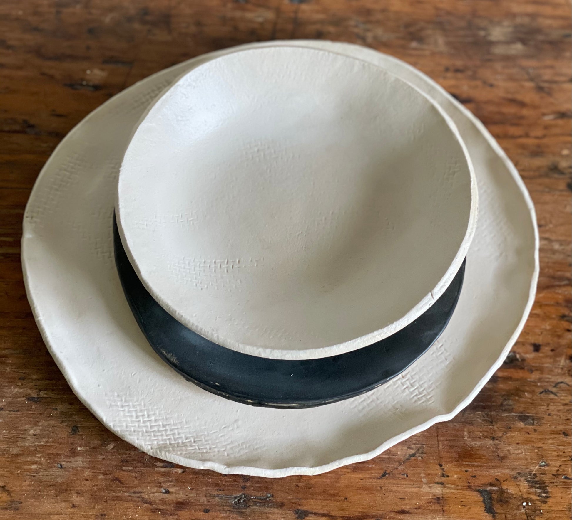 Handmade matte white dinner plate with smaller black dessert plate on top and a matte white bowl stacked on top of both plates.
