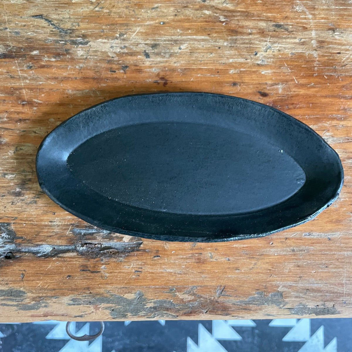 A black matte oval ceramic trinket dish placed on a wooden surface.