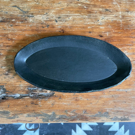 A black matte oval ceramic trinket dish placed on a wooden surface.