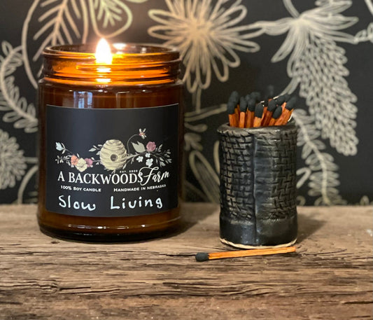 A handmade ceramic matchstick holder in matte black, displayed next to a lit candle, with a few matchsticks placed in it.