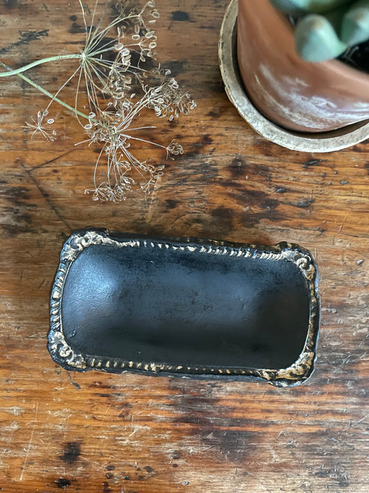 Handmade rustic pottery dish in black matte finish with vintage design, placed on a wooden surface.
