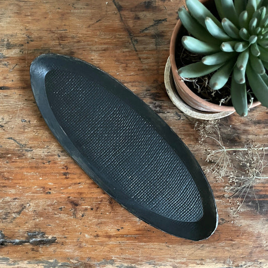 Black oval object on a wooden surface with a potted plant